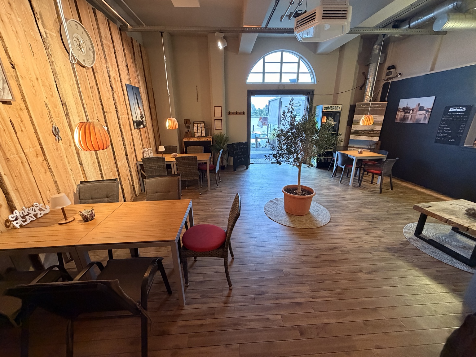 Unser Café im Pierspeicher mit Holztischen, warmen Lampen und Blick zum Hafen
